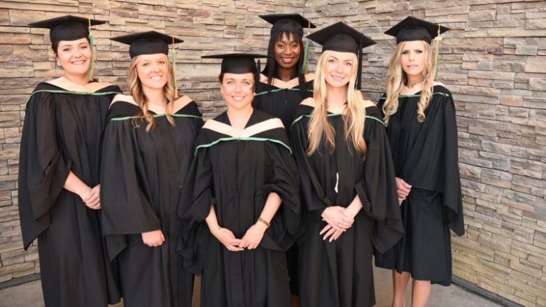 A group of women dressed in graduation gowns stand together,.