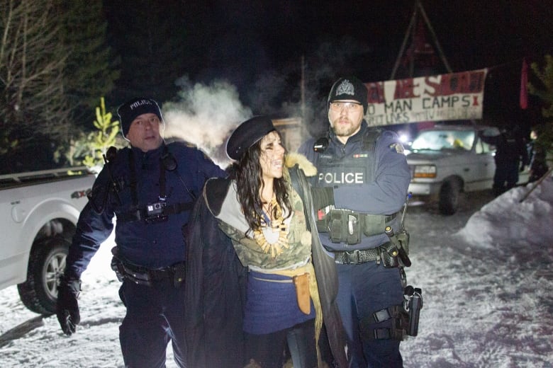 A woman is handcuffed and removed by police against a snowy background.
